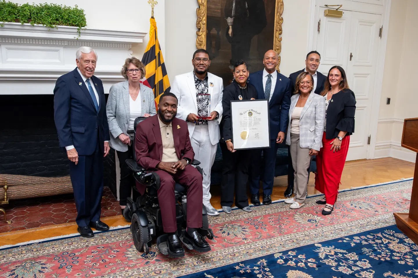 Eric and Linda holding an award and framed proclamation at a ceremony with other attendees.